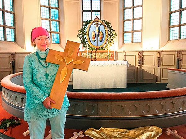 Ingela st&aring;r framme vid altaret och h&aring;ller K&auml;rlekens Kors i famnen